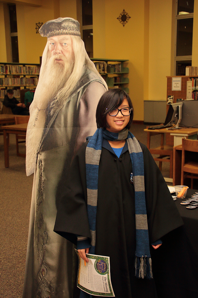 Attendee dressed in Hogwarts robes posing with Dumbledore cutout