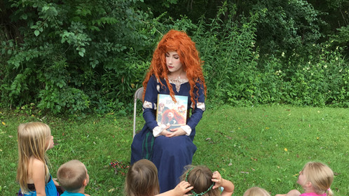 Merida reads to group of children in outdoor setting