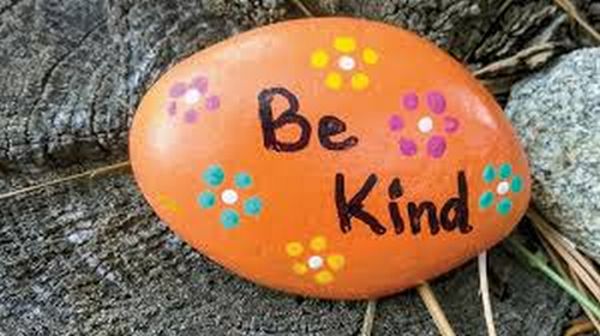 Orange painted rock with flowers and words "Be Kind" on it
