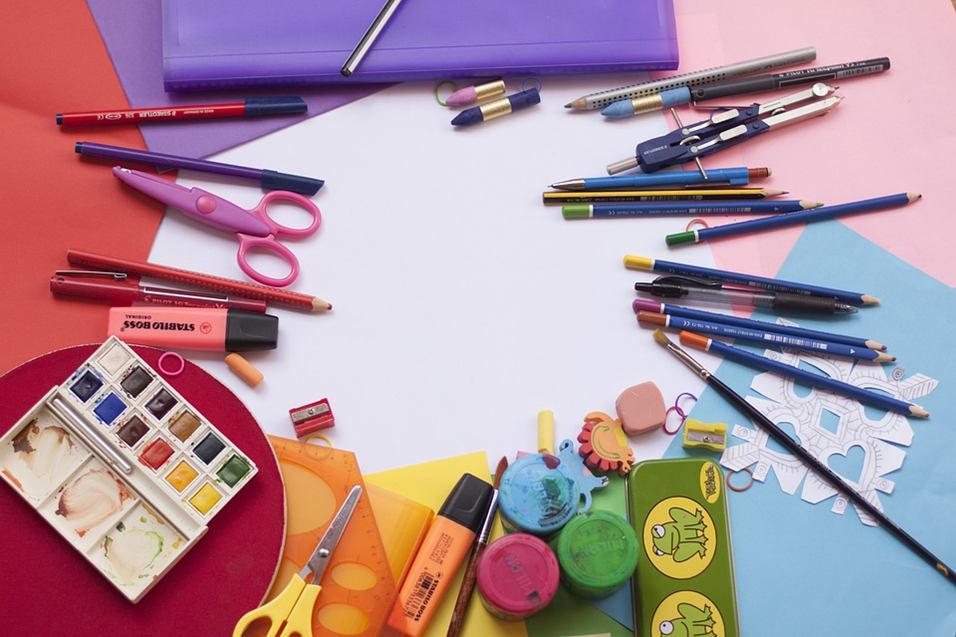 a variety of colorful craft supplies arrance in a circle including paper, pens, water colors paint brushes, punches
