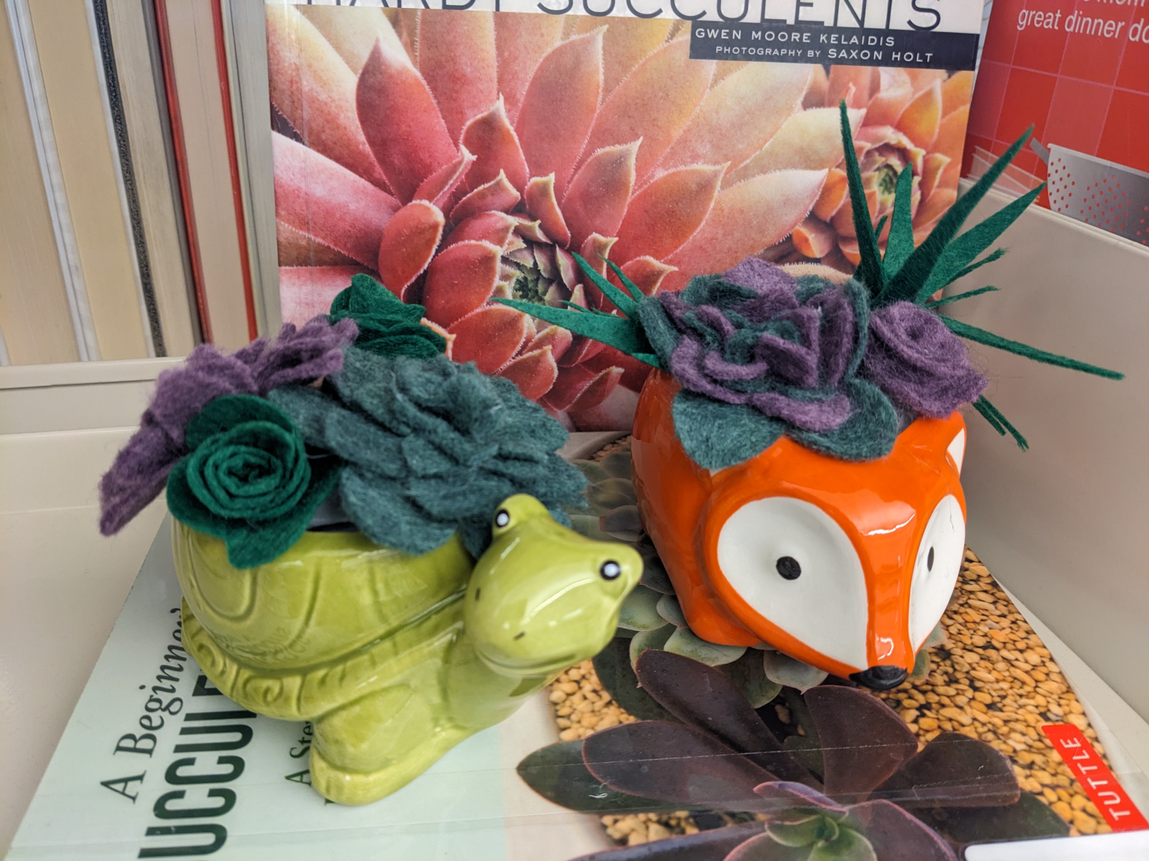 Small green turtle and orange and white fox shaped planters with green and purple felt succulents displayed with colorful succulent photo books