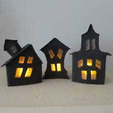 Three black haunted houses made of cardboard with lighted windows