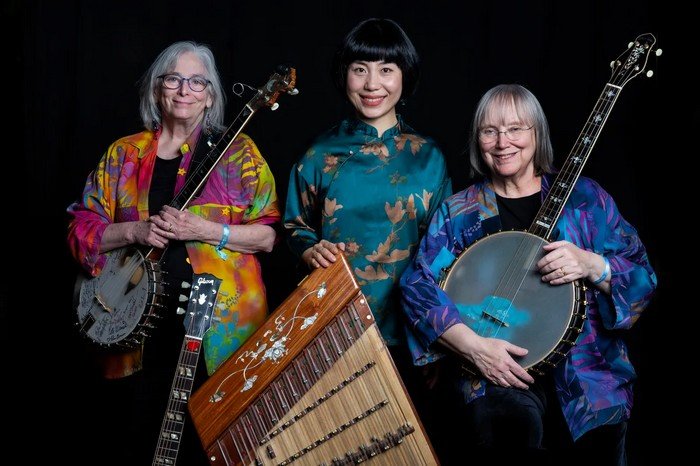 Three women in colorful outfits, each holding a musical instrument.