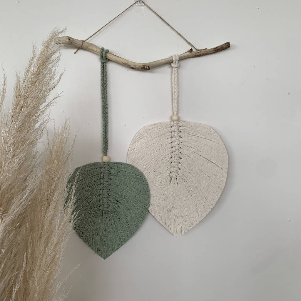 two macrame leaves hanging from a branch on a wall