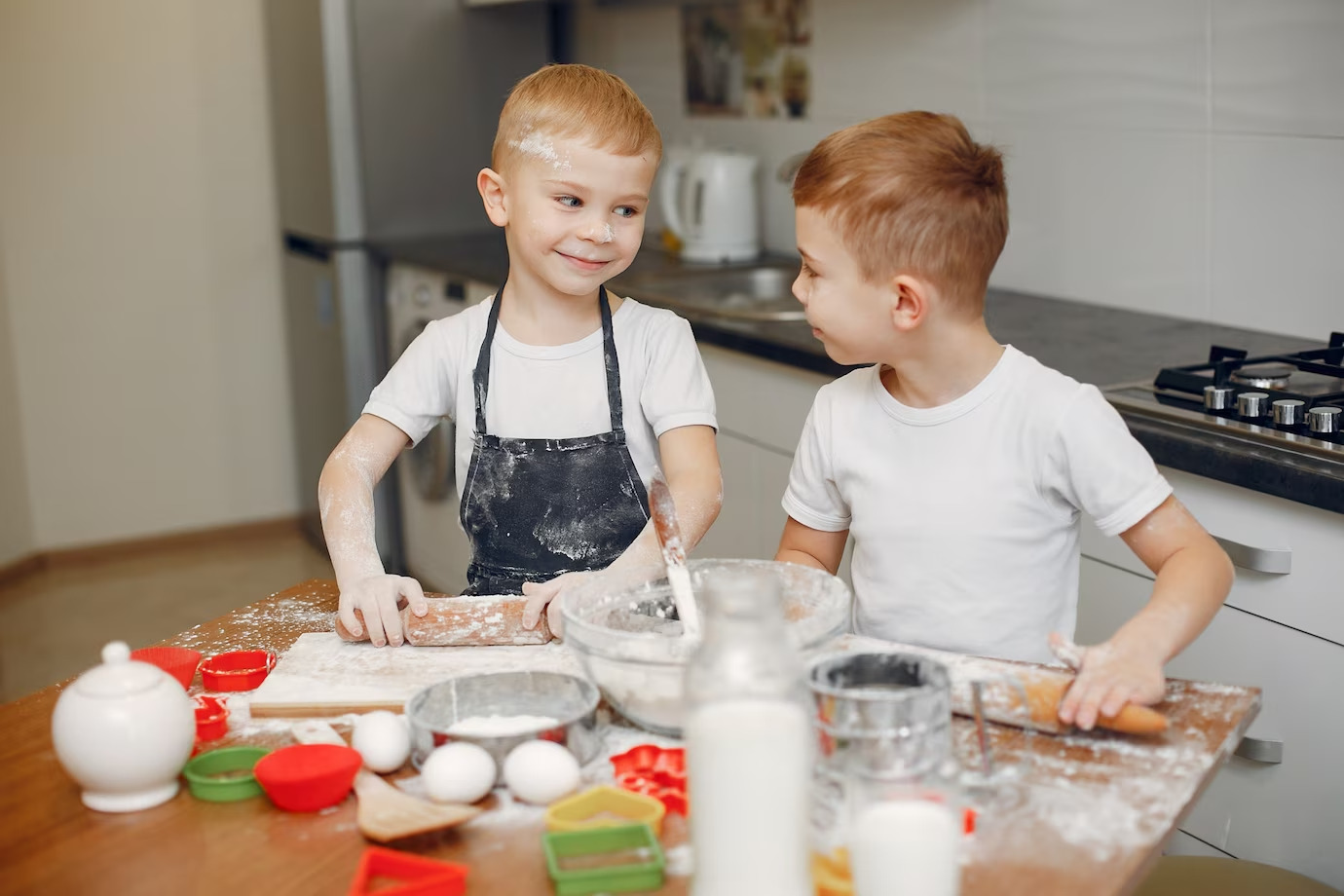 Two boys rolling out dough at table with cooking supplies