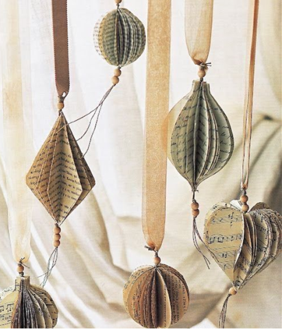 Several holiday ornaments made cut and folded book pages and sheet music in a variety of simple shapes, hanging by neutral velvet ribbon