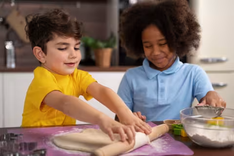 Two children, one in yellow & one in blue, cooking together