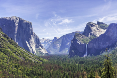 Wide view of mountains and forest with a waterfall in the distance. 