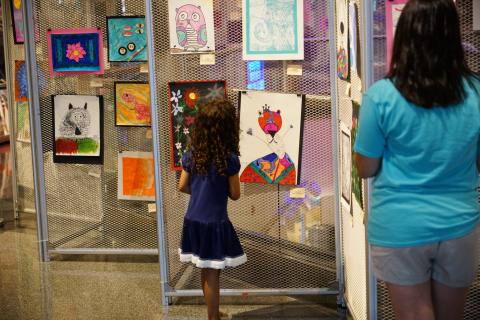 Children's art displayed on wire screens with child and adult viewing