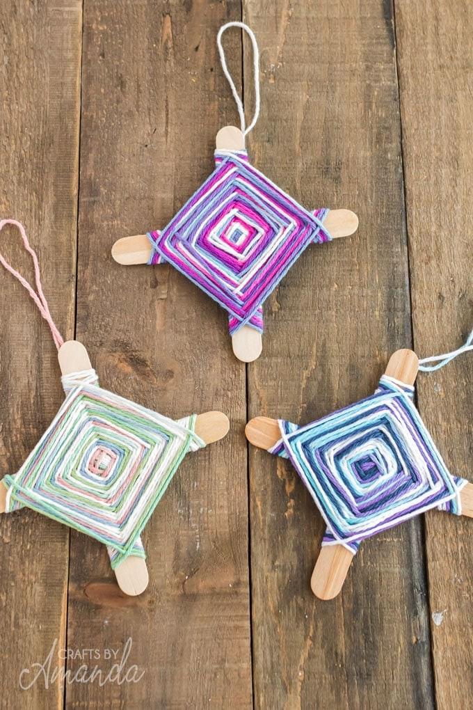 Three different color yarn & stick Ojo de Dios against brown background